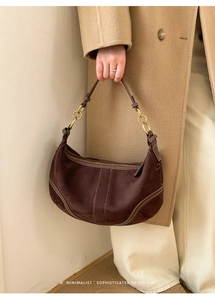 Détail du sac demi-lune en daim marron foncé avec surpiqûres blanches et anneaux dorés