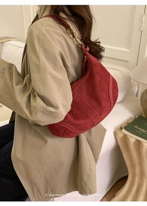 Détail du sac bandoulière demi-lune en daim rouge avec surpiqûres et anneaux métalliques