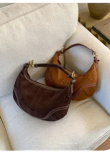 Détail de sacs hobo en daim avec surpiqûres blanches et boucle dorée sur un canapé doux