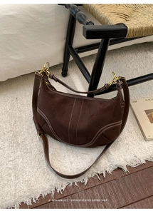 Détail du sac demi-lune en daim marron foncé avec surpiqûres blanches et boucles dorées