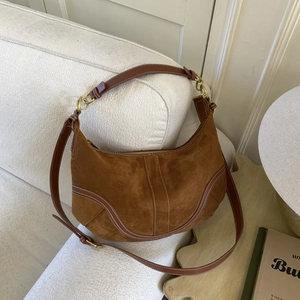 Sac demi-lune en daim marron avec surpiqûres blanches sur un canapé en tissu beige