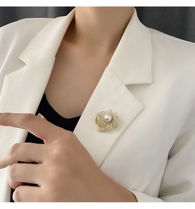 Detailed close-up of a luxury gold brooch with pearl and zircons on a white blazer lapel