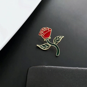 Artistic red rose enamel pin with gold plating on minimalist black textured backdrop
