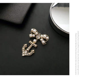 Macro detail of golden bow brooch with pearls and zircon-set anchor pendant