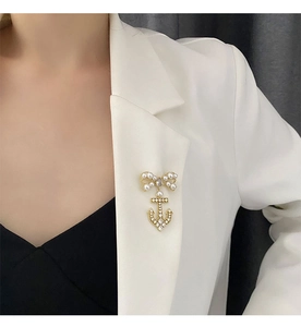 Elegant gold bow brooch with pearl and anchor pendant shown on a white blazer