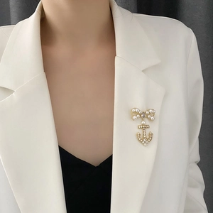 Elegant gold bow and anchor brooch with pearls and zircon crystals on white blazer