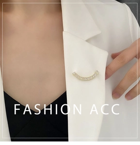 Détail de la broche dorée avec pierres baguette sur le revers d'un blazer blanc