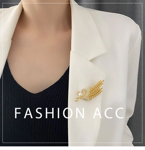 Détail d'une broche épi de blé dorée avec perle et zircons sur un blazer blanc