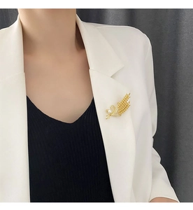 Vue détaillée d'une broche épi de blé dorée avec perles sur revers de veste blanc