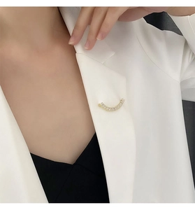 Détail d'une élégante broche sourire dorée avec zircons sur un blazer blanc