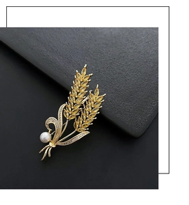 Détail d'une broche en épi de blé doré avec pierres jaunes et perle sur fond noir texturé