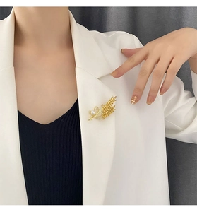 Détail macro d'une broche épi de blé dorée avec perle et cristaux sur revers blanc