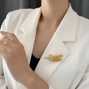Broche épi de blé dorée avec perle et cristaux sur le revers d'un blazer blanc