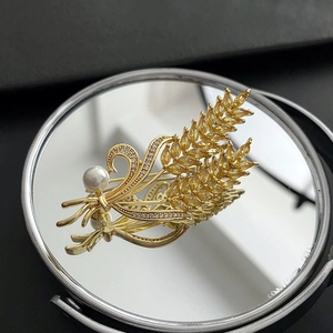 Broche épi de blé dorée élégante avec zircon jaune et perle sur une surface miroir