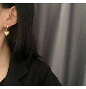 Nahaufnahme eines goldenen Herzohrrings mit Perlmutt-Inlay, getragen von einem Modell