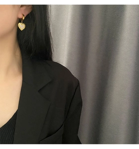 Detail von herzförmigen Goldohrringen mit Muscheltextur am Ohr getragen von Model