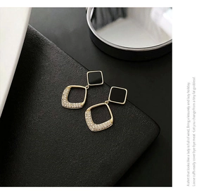Detail shot of geometric gold earrings with black enamel and zircon pavé on leather