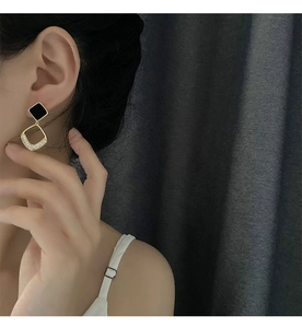 Detail of geometric drop earring with black square stud and zircon-set gold pendant
