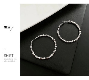 Macro detail of silver hoop earrings featuring textured geometric metallic beads
