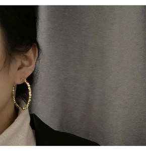 Close-up of golden geometric faceted hoop earrings worn on a model in minimalist style