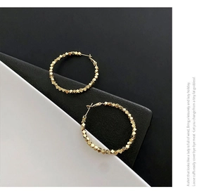 Detail of gold hoop earrings with faceted beads on a black and white background