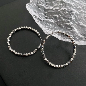 Silver textured hoop earrings with faceted geometric beads on a minimalist dark background