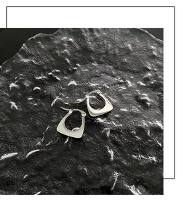 Vista macro di orecchini geometrici a U in titanio argento lucido su pietra