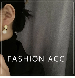 Close-up of elegant gold arc earrings with white pearls worn by model on dark background