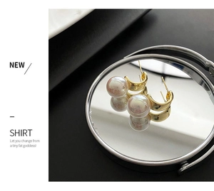 Detailed view of gold arched pearl earrings reflecting on a mirror surface