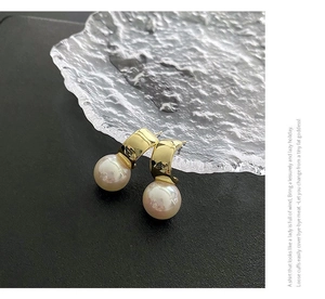 Macro shot of elegant gold arc earrings with white pearls on a textured stone base