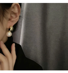 Detail of elegant gold curved metal earrings with large white pearl on a person's ear