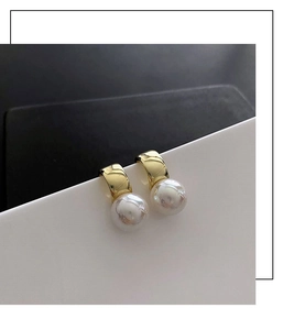 Close-up of elegant gold arc earrings with large pearls on geometric background
