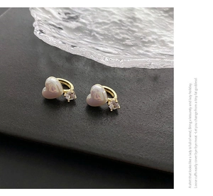 Gros plan de boucles d'oreilles cœur dorées avec perle irisée et zircon brillant