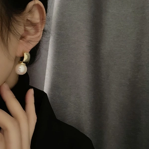 Elegant gold curved metal earrings with large round pearls shown on ear model