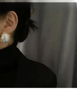 Close-up of model wearing large pearl earrings with wavy gold metal trim on black suit