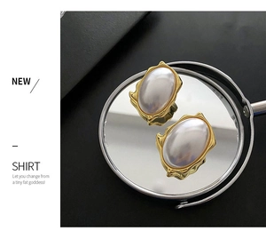 Close-up of luxury pearl earrings with vintage gold textured edge on a mirror surface