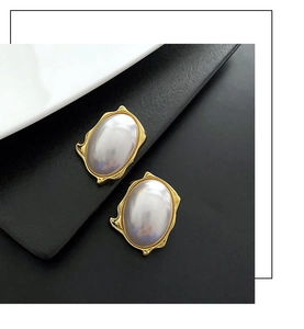 Detail of French vintage pearl earrings with irregular gold wavy edges and white oval beads