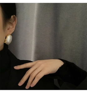 Macro shot of large oval pearl earrings with wavy gold edges worn by a model