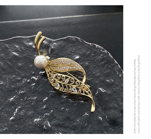 Detailed close-up of leaf brooch with pearls and zircon crystals on a black stone tray