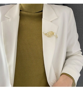 Detail view of a gold leaf brooch with white pearl and diamonds on white suit lapel