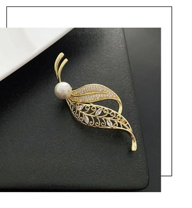 Detail of leaf-shaped gold brooch featuring a large white pearl and zircon accents