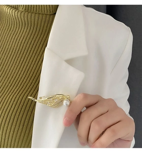 Detailed view of a gold leaf brooch with pearls and crystals on a white blazer lapel
