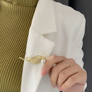 Elegant gold leaf brooch with large pearl and sparkling crystals on white blazer lapel