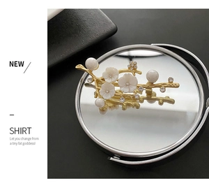 Detailed view of golden branch brooch with white shell flowers and pearls on reflection