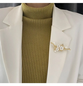 Detailed view of a golden plum branch brooch with white shells and pearls on a white blazer