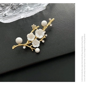 Detailed view of floral brooch with white shell petals and pearls on golden branch