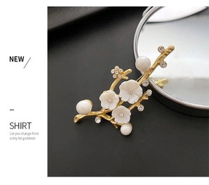 Detail of elegant gold flower brooch with white shell petals and pearls on black surface