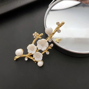 Elegant gold flower branch brooch with shell petals and pearls on a black background