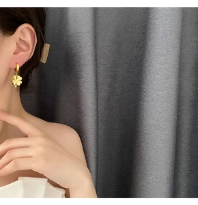 Close-up of gold clover hoop earrings worn by a model against a grey background