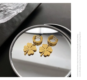 Detailed close-up of golden clover dangle hoops on a reflective silver surface